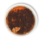 Top view of brewed Caravan of Palmyra loose leaf black tea in a white cup, showing amber liquor with floating fig and almond pieces.
