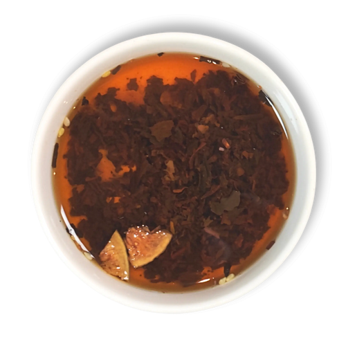 Top view of brewed Caravan of Palmyra loose leaf black tea in a white cup, showing amber liquor with floating fig and almond pieces.