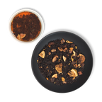 Brewed Caravan of Palmyra black tea beside dry loose leaf blend with figs, dates, almonds and sesame on a black plate.