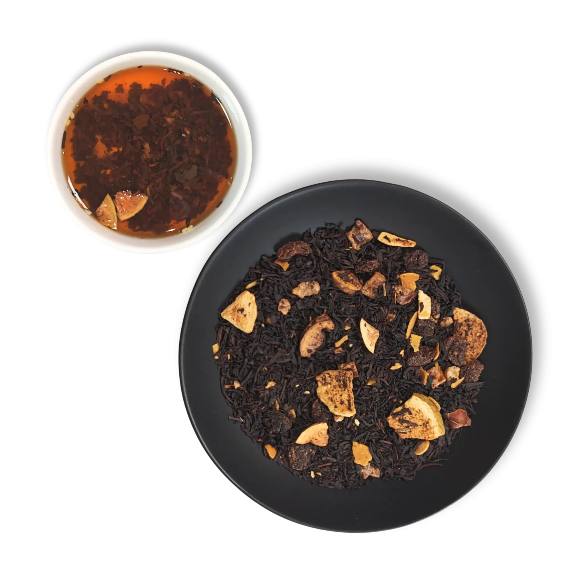 Brewed Caravan of Palmyra black tea beside dry loose leaf blend with figs, dates, almonds and sesame on a black plate.