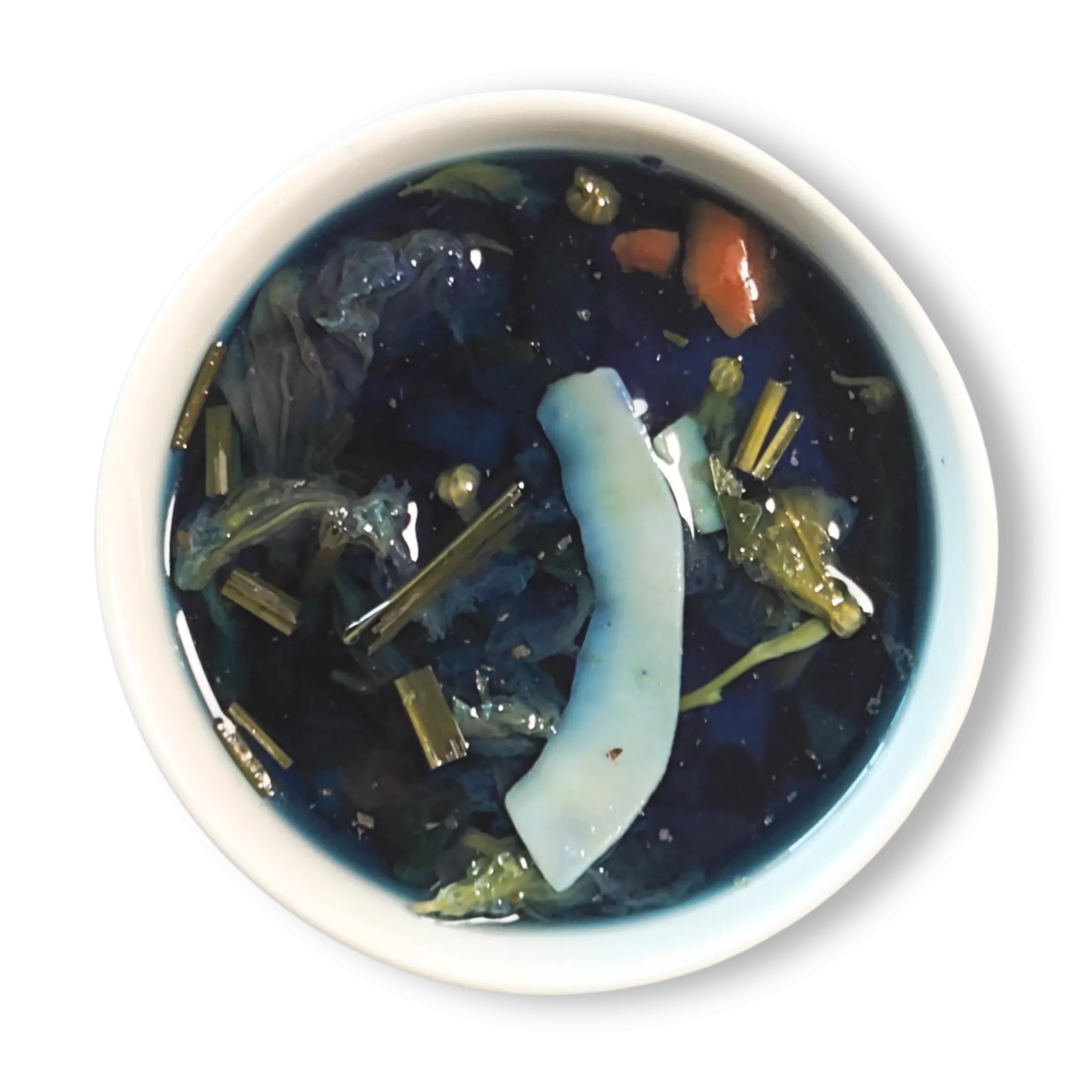 Azure Alchemy golden blue herbal tea infusion in white cup, vibrant deep blue color with lemongrass and coconut pieces floating