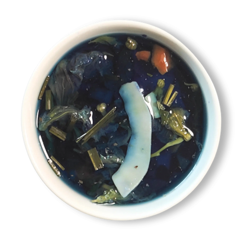 Azure Alchemy golden blue herbal tea infusion in white cup, vibrant deep blue color with lemongrass and coconut pieces floating