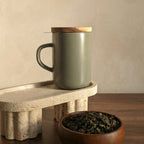 Minimal Almond green stoneware Juliet mug with closed acacia wood lid on a terrazzo stand.