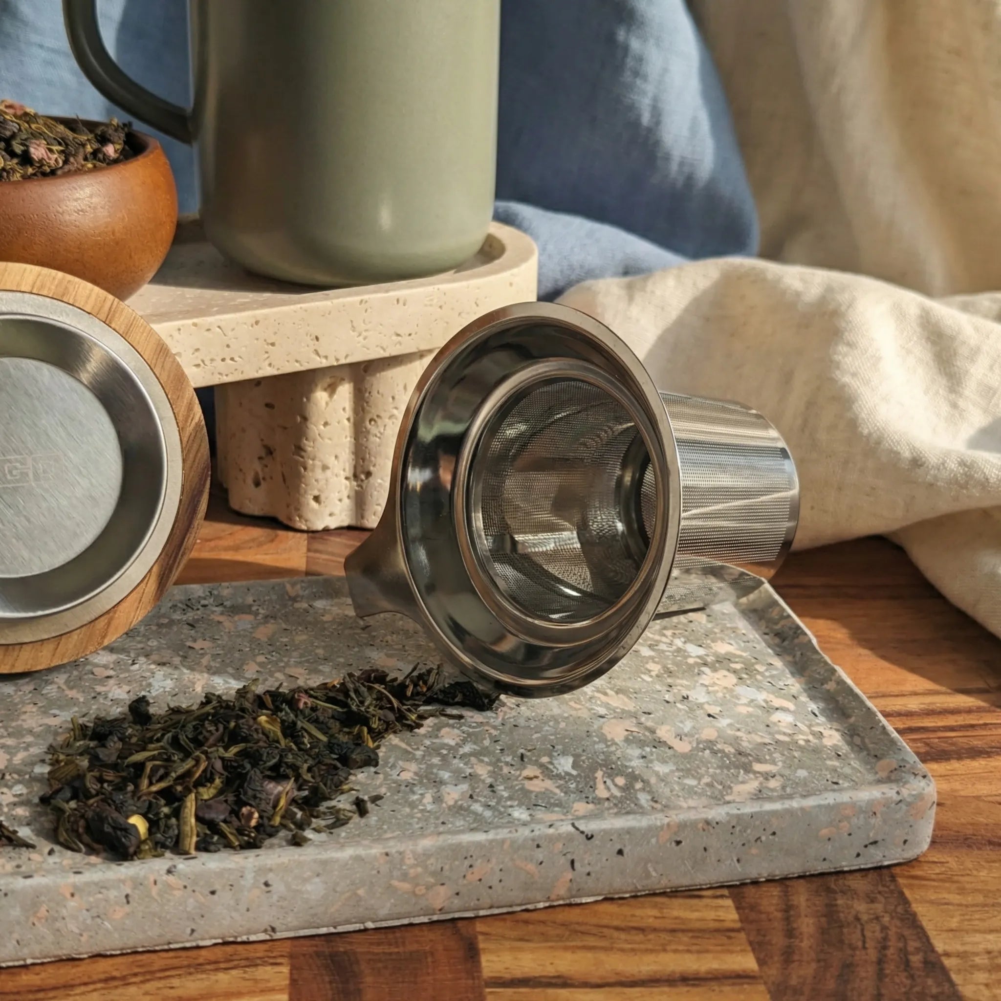 Detail of fine mesh stainless steel infuser for loose-leaf tea with Almond mug in background.