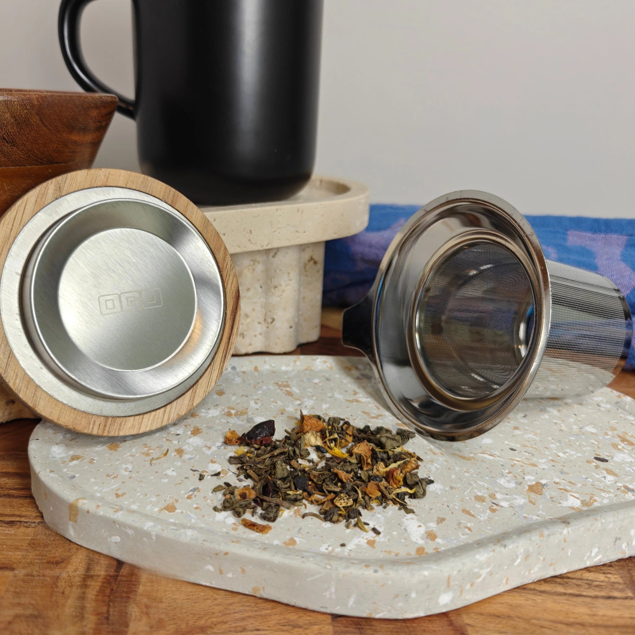 Underside of acacia lid showing OGO logo and stainless steel tea infuser displayed in front of black mug.