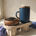 Deep Blue stoneware Juliet mug with closed acacia wood lid for heat retention sitting on a terrazzo stand.