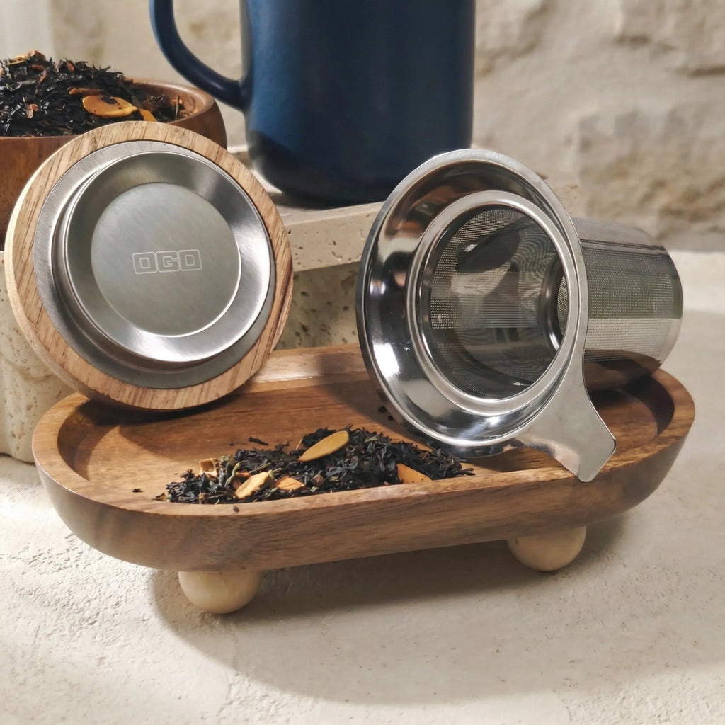 Underside of acacia lid showing OGO logo and stainless steel tea infuser displayed in front of Blue mug.