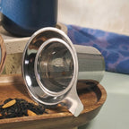 Detail of fine mesh stainless steel infuser for loose-leaf tea with Juliet Blue mug in background.