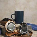Juliet Blue Stoneware Tea Mug 475ml with stainless steel infuser and acacia lid next to loose-leaf tea.