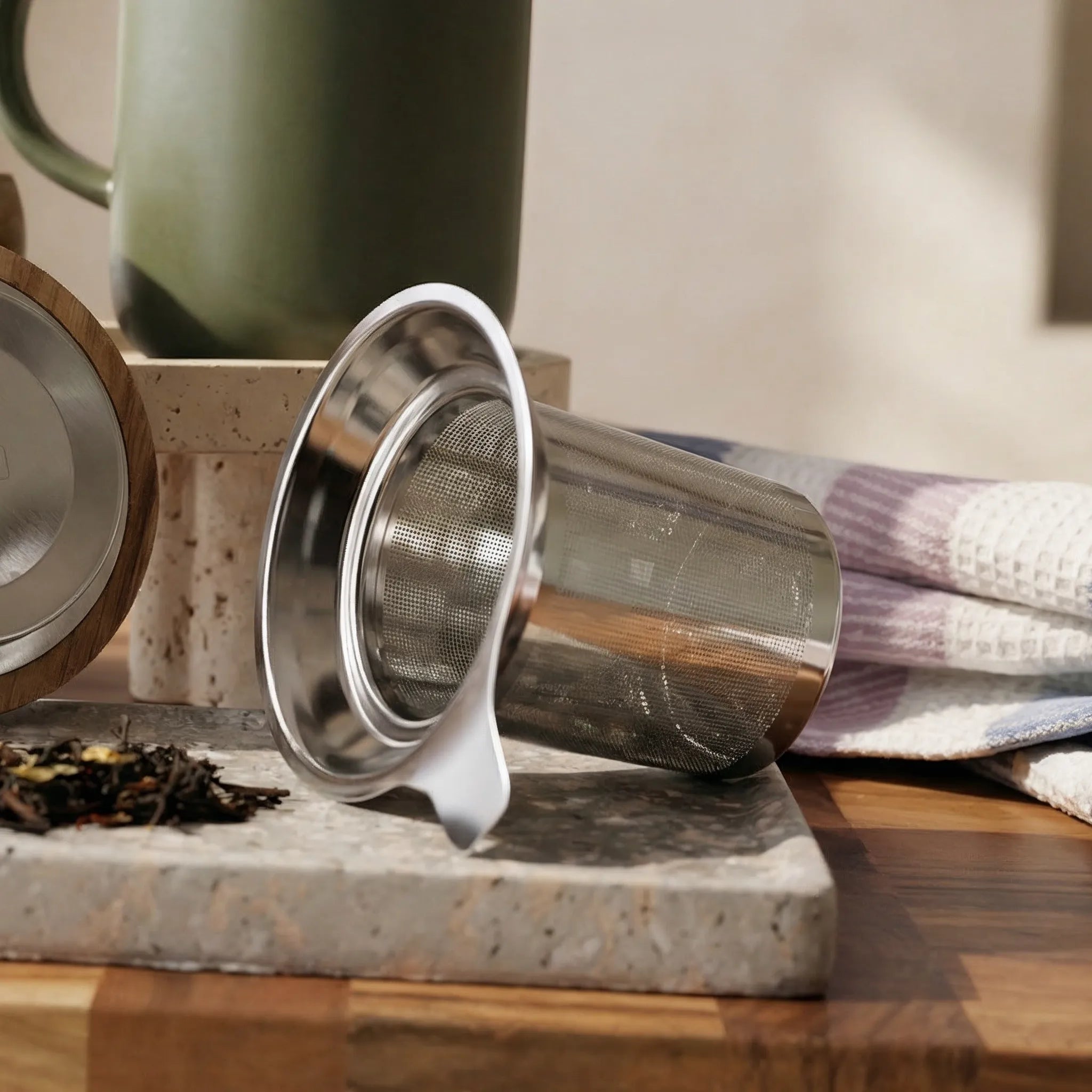 Detail of fine mesh stainless steel infuser for loose-leaf tea with Khaki green mug in background.