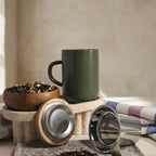 Juliet Khaki Stoneware Tea Mug 475ml with stainless steel infuser and acacia lid next to loose-leaf tea.