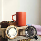 Juliet Paprika Stoneware Tea Mug 475ml with stainless steel infuser and acacia lid next to loose-leaf herbal tea.