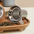 Detail of fine mesh stainless steel infuser for loose-leaf tea with Perle grey mug in background.