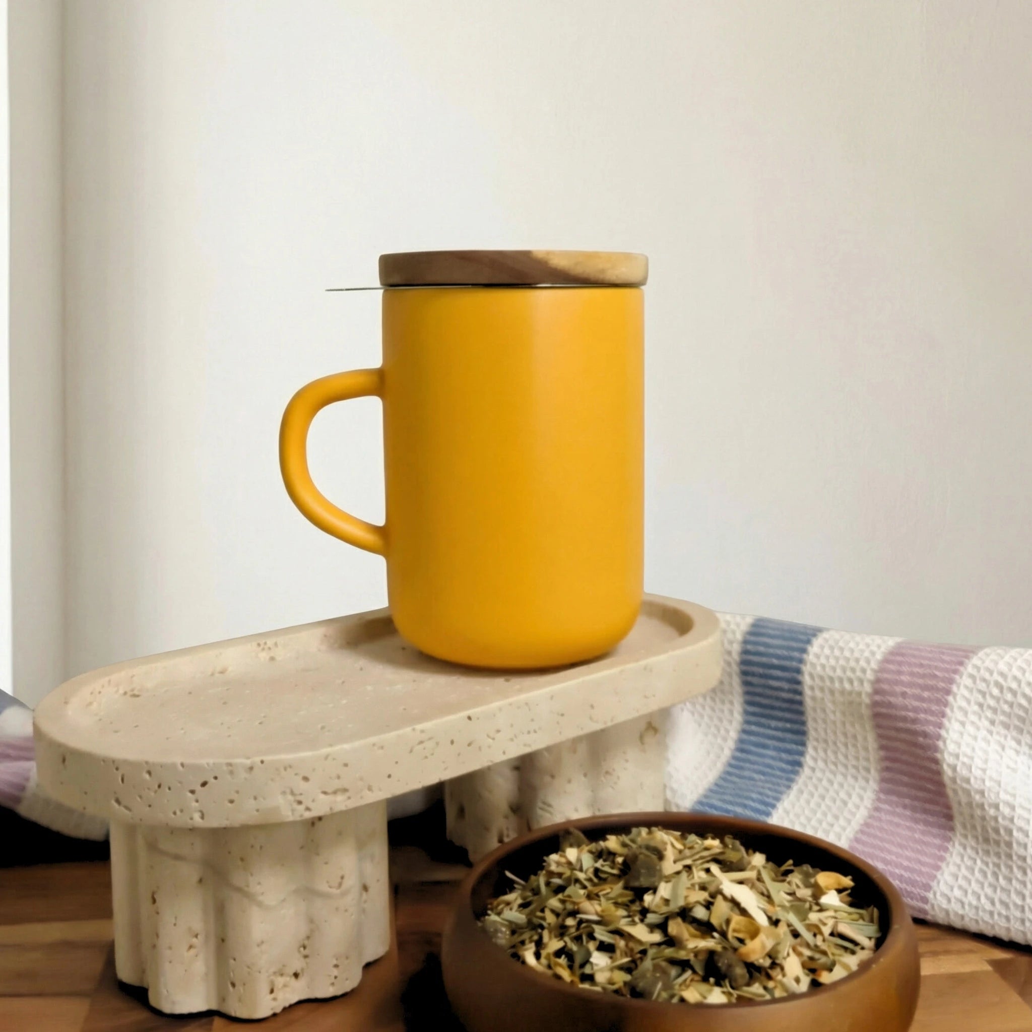 Yellow stoneware Juliet mug with closed acacia wood lid for heat retention sitting on a terrazzo stand.