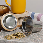Underside of acacia lid showing OGO logo and stainless steel tea infuser displayed in front of yellow mug.