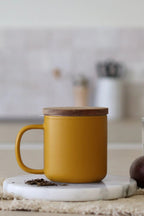 Juliet Yellow 300 ml tea mug with acacia lid on a table with loose-leaf tea