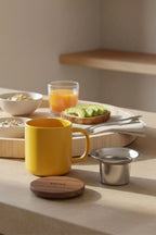 Juliet Yellow 300 ml tea mug with acacia lid on a table with loose-leaf tea